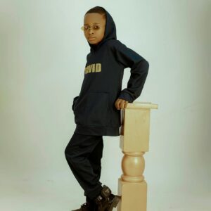 A fashionable young boy poses in a hoodie and sunglasses, showcasing cool style.