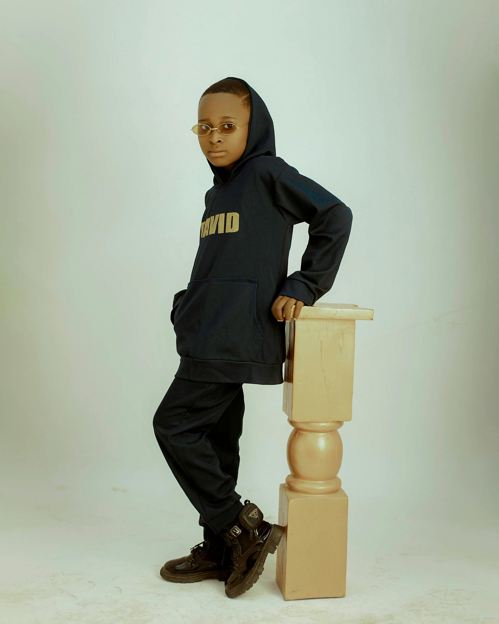 A fashionable young boy poses in a hoodie and sunglasses, showcasing cool style.