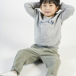 Cute little Asian boy in trendy casual clothing sitting on floor in studio