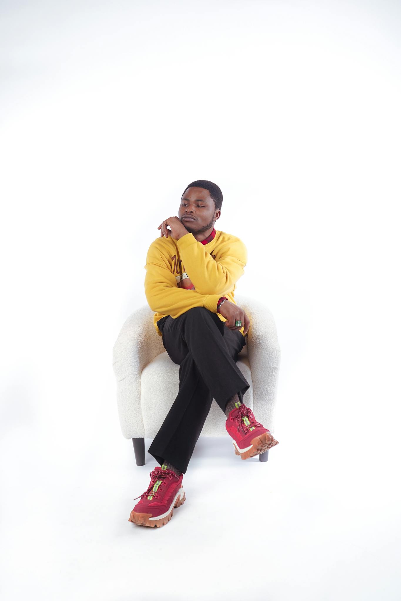 Fashionable man in yellow sweatshirt and red sneakers sitting on a white armchair with a white background.