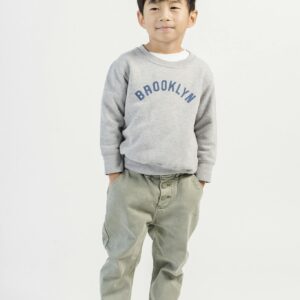 Full body of adorable Asian boy with hands on pockets wearing casual jeans and sweatshirt with sneakers in white studio